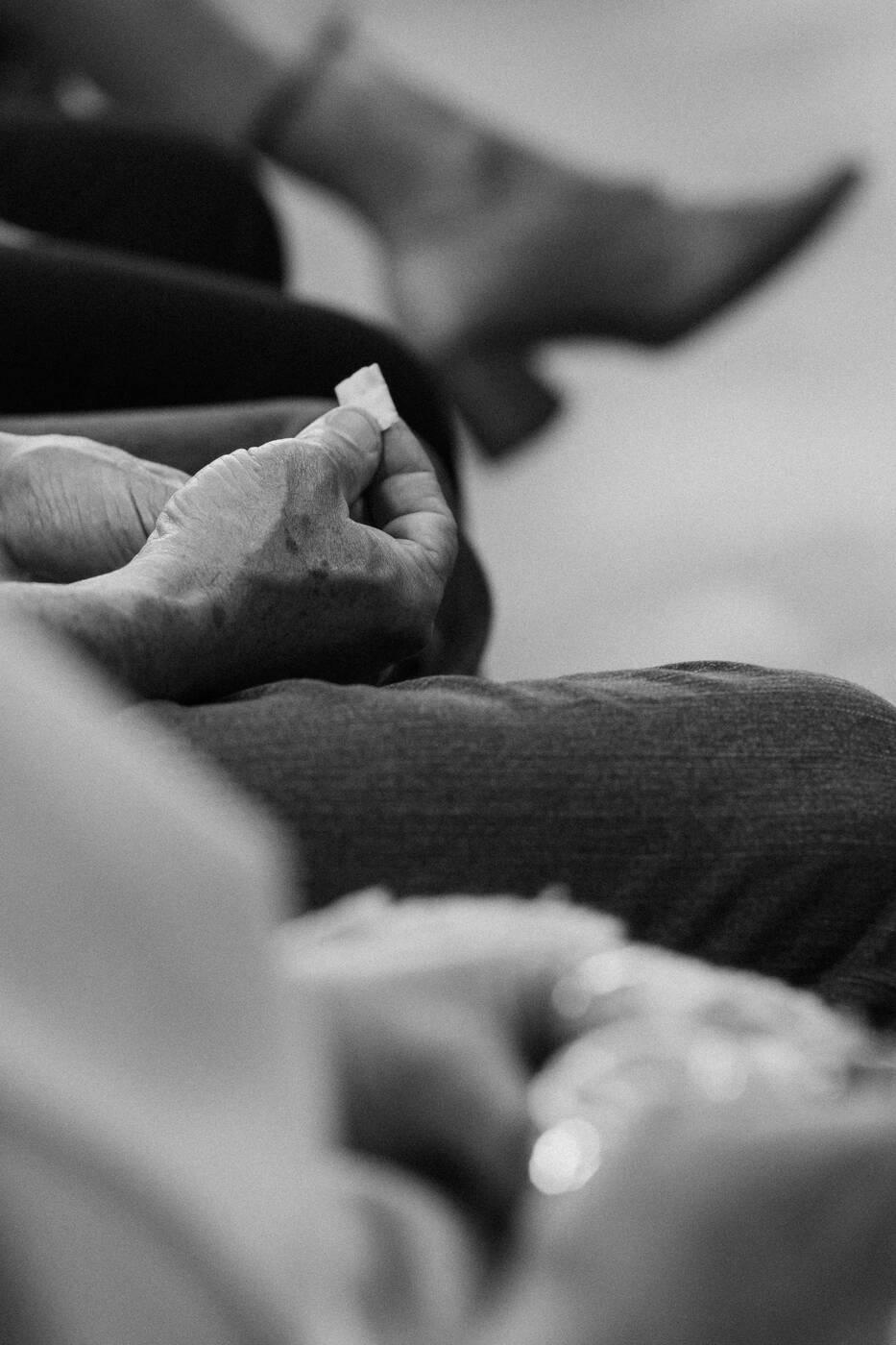 Mãos de uma pessoa idosa durante o culto, em preto e branco